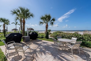 An outdoor patio with a view of the beach, including a grill, seating area, and umbrellas. - Gulffront Paradise at Vacation Villa (Fort Myers Beach)