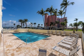 A swimming pool with lounge chairs and palm trees. - Gulffront Paradise at Vacation Villa (Fort Myers Beach)