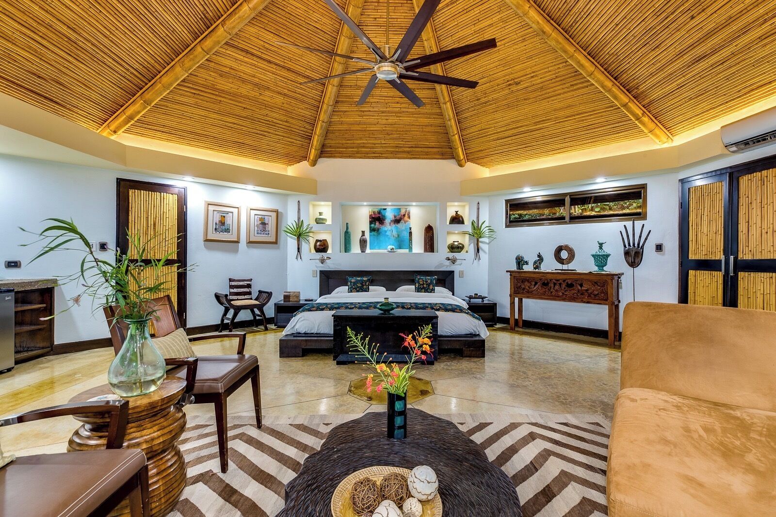 A spacious room with a bed, a sofa, a dining table, and a ceiling fan.