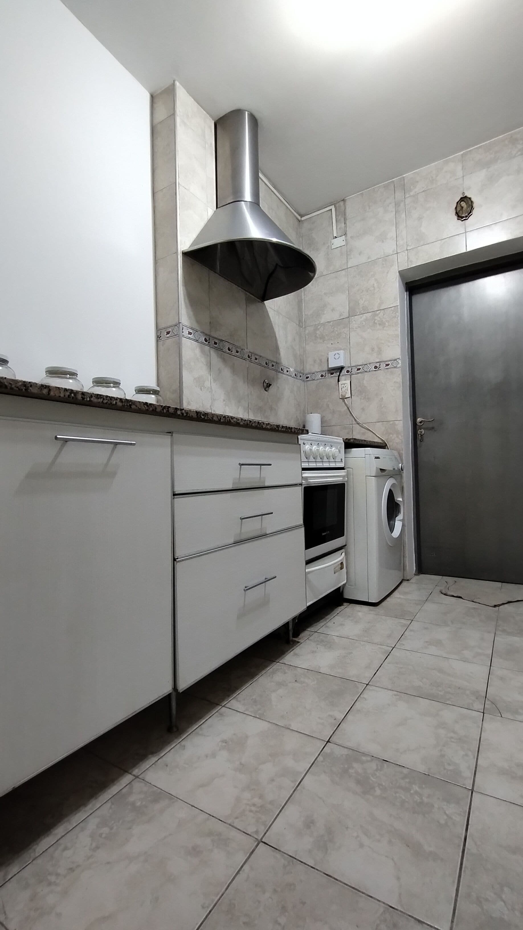 Una cocina con campana extractora de acero inoxidable, horno empotrado, lavadora y una puerta.