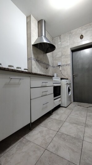 A kitchen with a stainless steel range hood, a built-in oven, a washing machine, and a door. - Vrbo Property (San Juan)