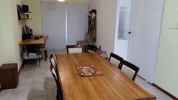 A dining area with a wooden table, chairs, a hanging light fixture, and a whiteboard.