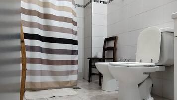 Un baño con inodoro, cortina de ducha y una silla.
