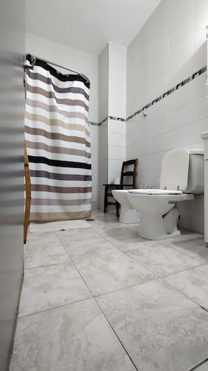 A bathroom with a toilet, a shower curtain, and a chair. - Vrbo Property (San Juan)