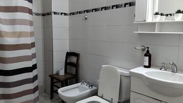 A bathroom with a toilet, bidet, and sink. There is a striped shower curtain and a chair.