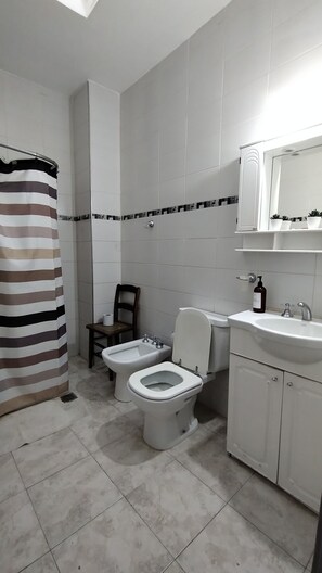 A bathroom with a toilet, bidet, and sink. There is a striped shower curtain and a chair.
