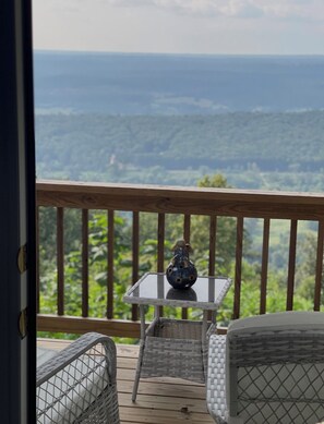 A balcony with a view of a forested landscape, a small table with a globe and a figurine, and wicker furniture. - Cozy 2-bedroom cottage in beautiful Mentone, AL family friendly modern amenities (Mentone)