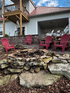 Ein Haus mit einem Steinkamin, vier roten Adirondack-Stühlen und einer überdachten Veranda.