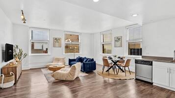 A modern living room with a sofa, a dining area with a table and chairs, and a kitchen with a dishwasher.