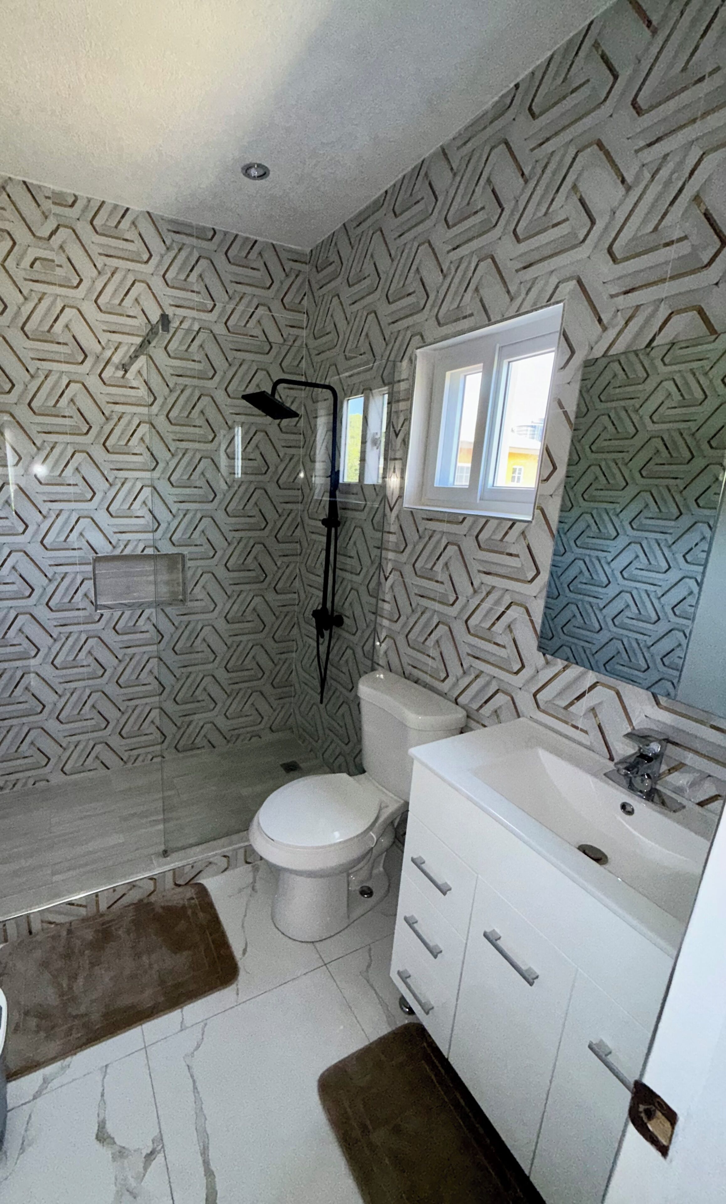 Et badeværelse med tapet på væggen, toilet, vask og brusebad.