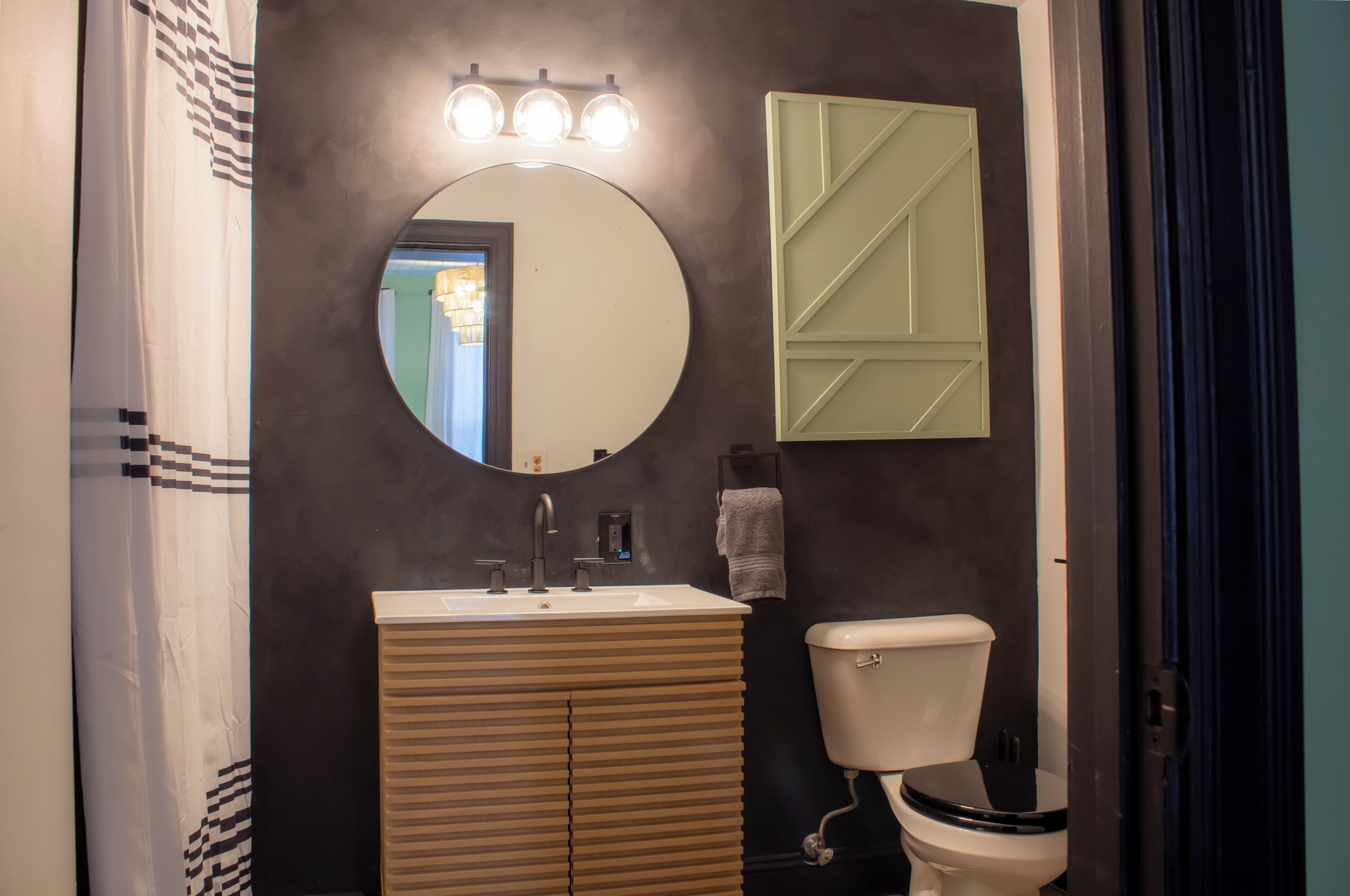 Un baño con un espejo redondo, un lavabo, un inodoro y un perchero para toallas.