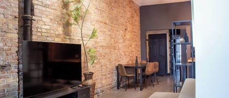 Una sala de estar con pared de ladrillo, un televisor de pantalla plana, una zona de comedor con sillas y un sofá.