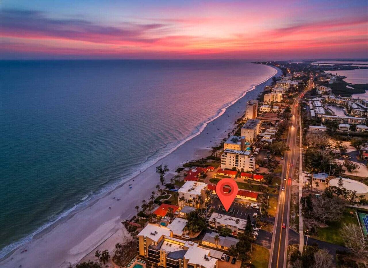 An aerial view of a coastal city with a beach, roads, and buildings.