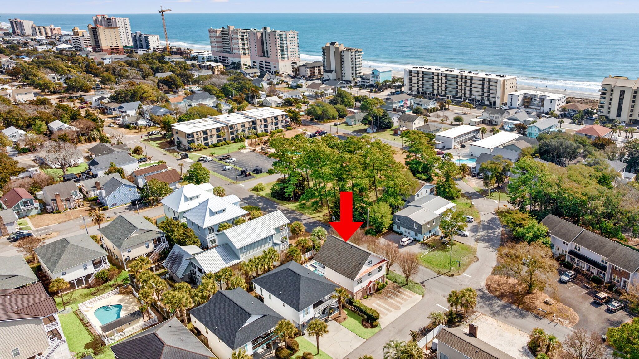 Vue aérienne d’une zone résidentielle côtière, avec des maisons, un grand hôtel et une plage en arrière-plan.