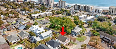 Vue aérienne d’une zone résidentielle côtière, avec des maisons, un grand hôtel et une plage en arrière-plan.