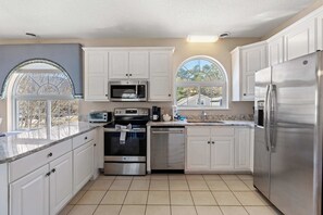 A modern kitchen with white cabinets, stainless steel appliances, a built-in microwave, and a window with a view of the outside. - North Myrtle | Sleeps 14 | Pool & Ping Pong (North Myrtle Beach)