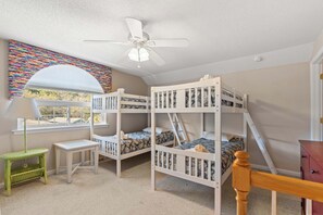 Ein Kinderzimmer mit Etagenbetten, einem Deckenventilator, einem Fenster mit Aussicht und einer farbenfrohen Wandmalerei.
