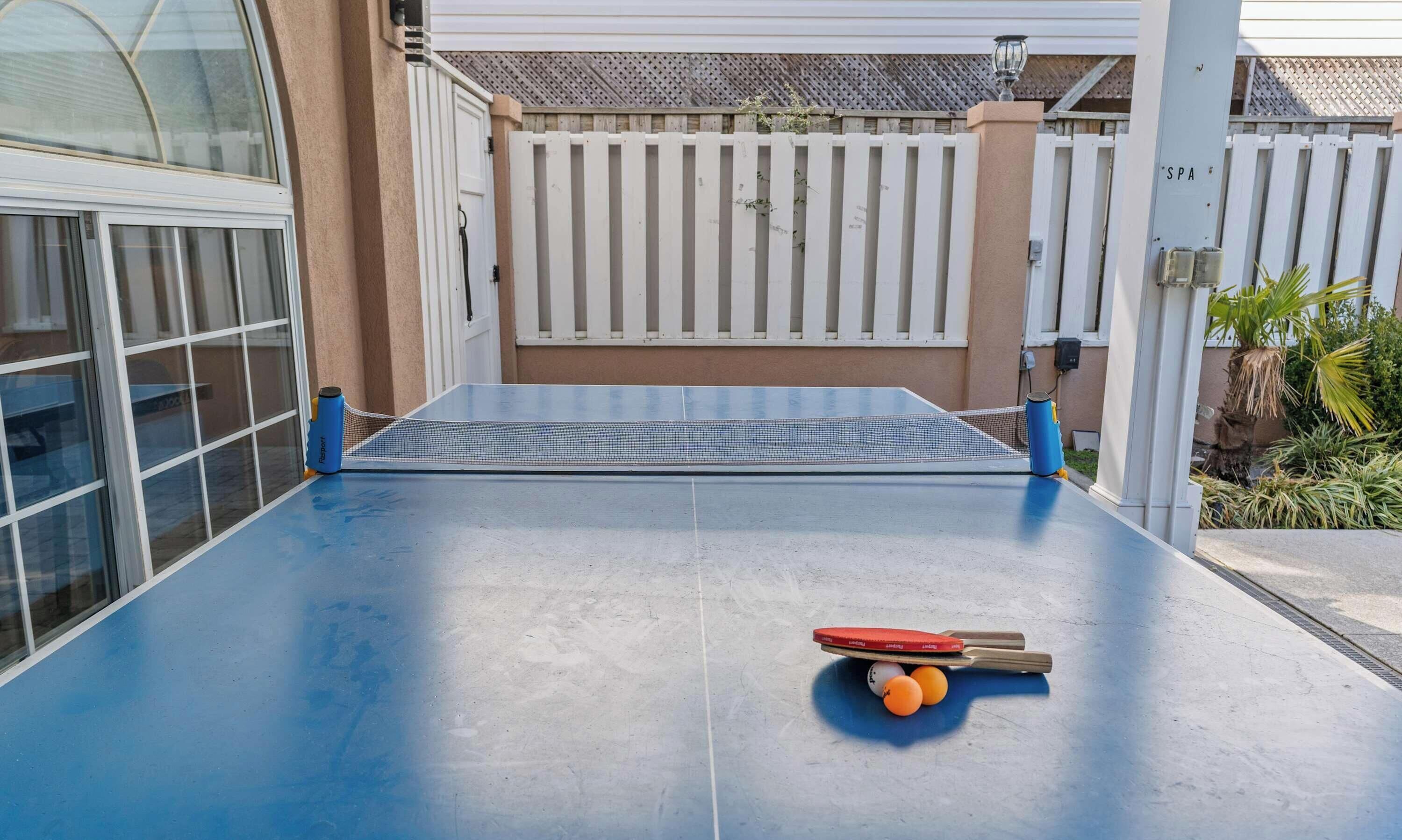 A ping pong table with a net, a paddle, and three balls.