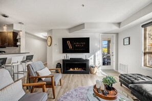 Un salon moderne doté d’une cheminée, d’un téléviseur fixé au mur et offrant une vue sur l’extérieur grâce à une porte.