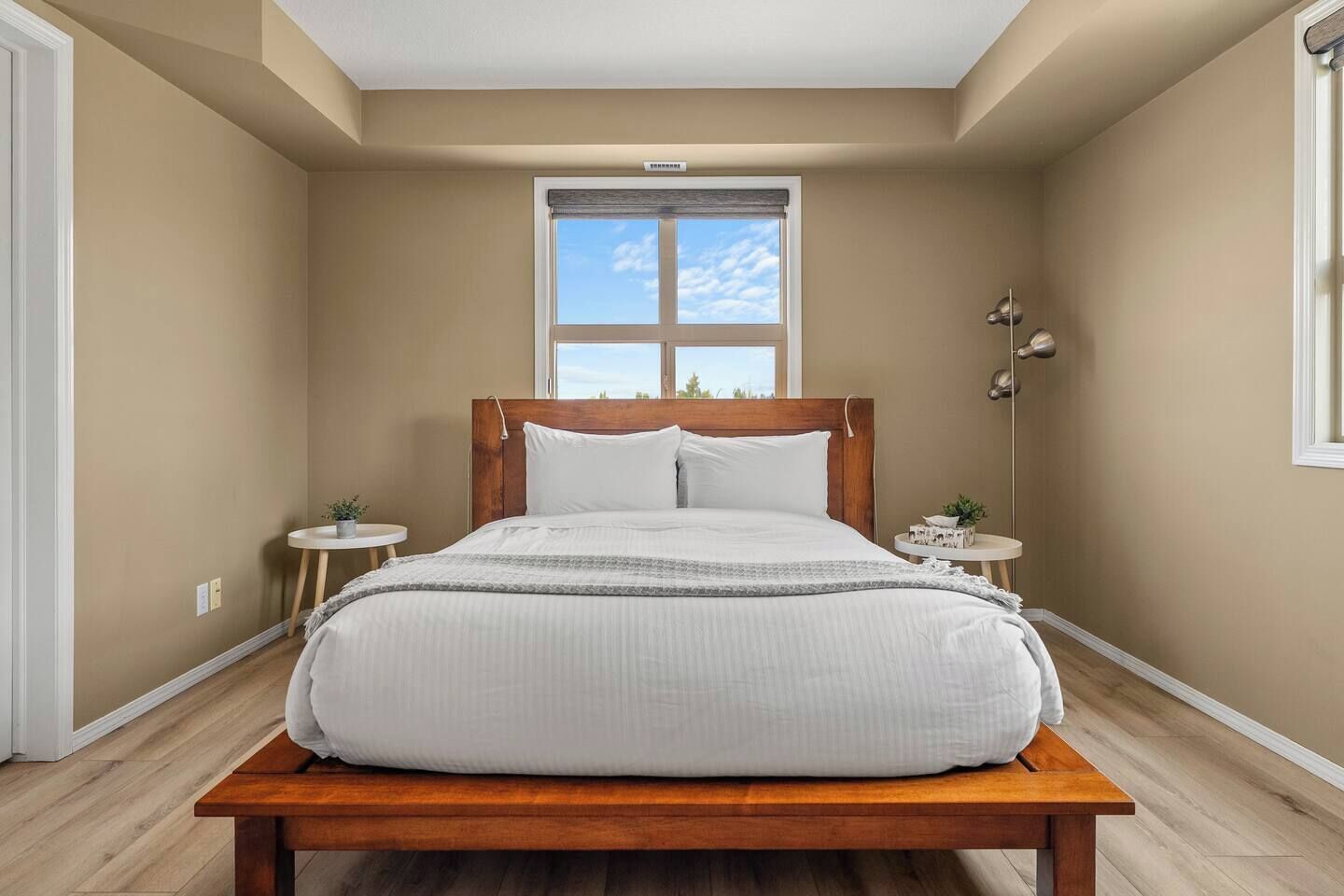 A bedroom with a wooden bed, two bedside tables, a window, and a ceiling light.