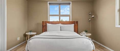 Une chambre à coucher avec un lit en bois, deux tables de chevet, une fenêtre et un luminaire au plafond.