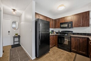 A kitchen with dark wood cabinets, a black refrigerator, a microwave, and a stove. - The Current | Outside Pool | Hot Tub | Gym | Pets (Invermere)