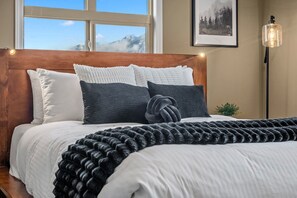 Un lit avec une tête de lit en bois, des oreillers blancs et gris foncé, et un plaid noir en tricot.