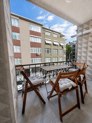 Een balkon met een tafel en twee stoelen, met uitzicht op een stadslandschap met hoge gebouwen.