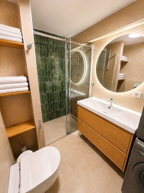 Een moderne badkamer met toilet, wastafel, spiegel en douche.