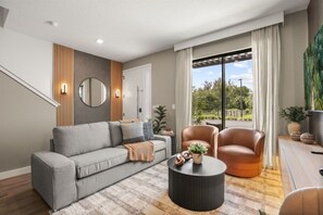 A modern living room with a grey sofa, a leather armchair, and a round coffee table. - 3 BD/ 3 BA/ The Hub at Westside Reserve - 3209 ED (Kissimmee)