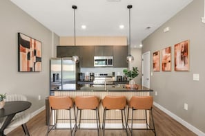 A modern kitchen with a central island, bar stools, and pendant lighting. - 3 BD/ 3 BA/ The Hub at Westside Reserve - 3209 ED (Kissimmee)