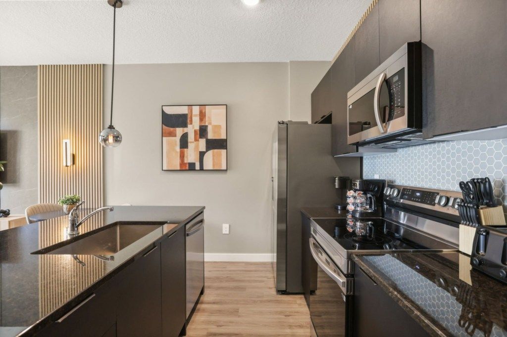 A modern kitchen with a central island, stainless steel appliances, and a contemporary light fixture.