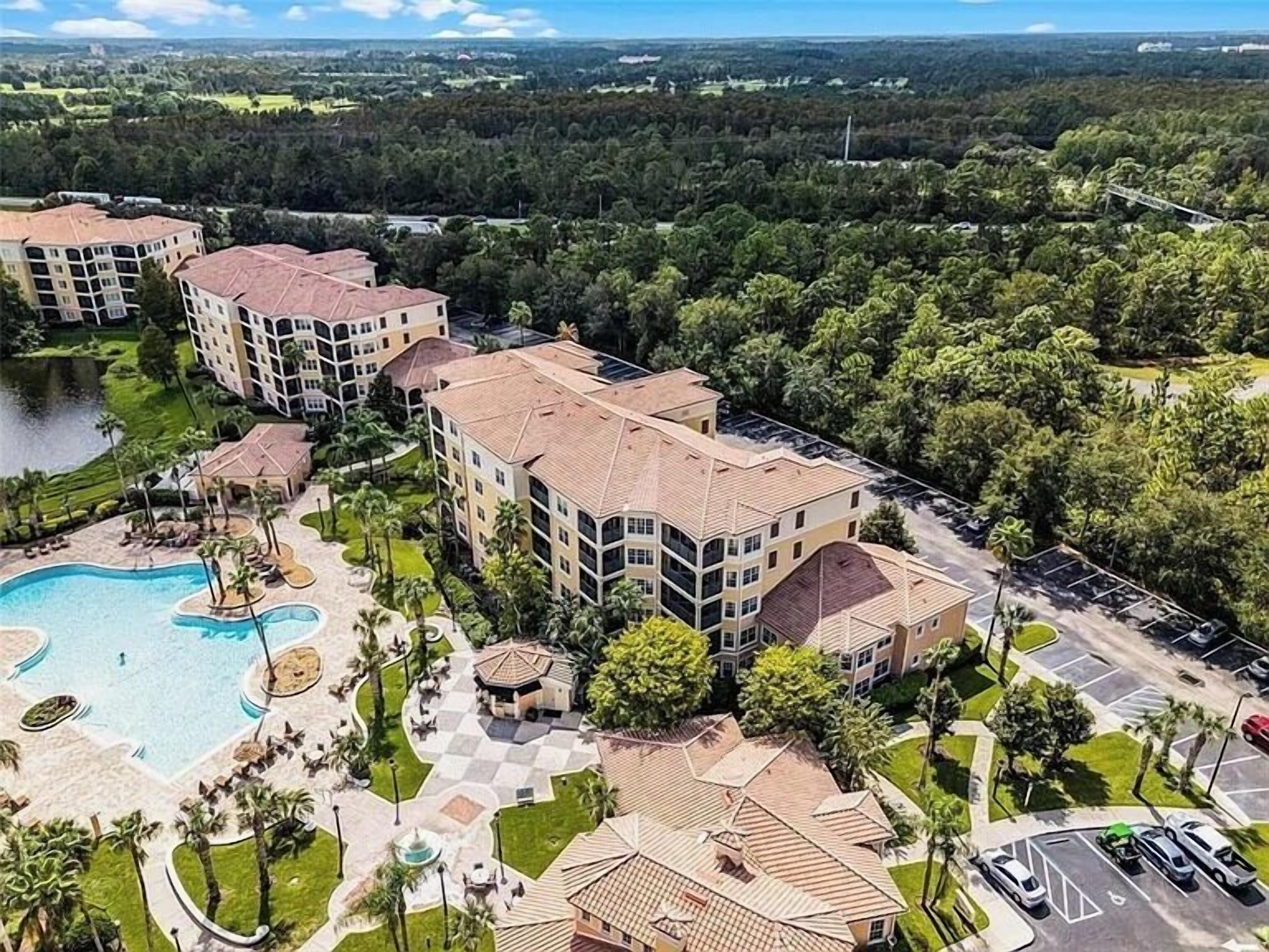 Un hotel de varios pisos con piscina, jardines ajardinados y zona de estacionamiento.