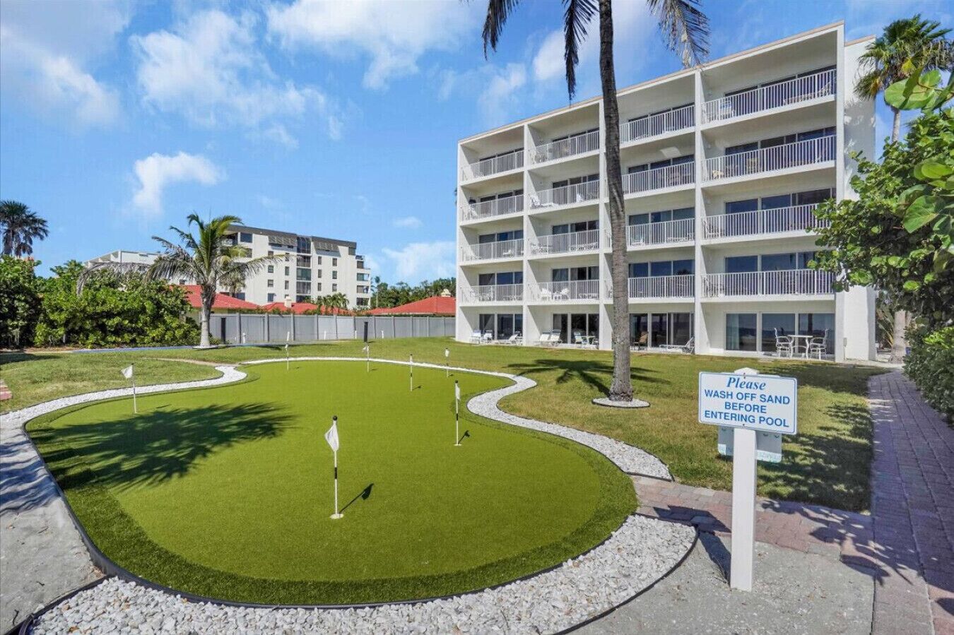 A hotel with a pool area, a sign instructing to wash off sand before entering the pool, and a well-maintained lawn.