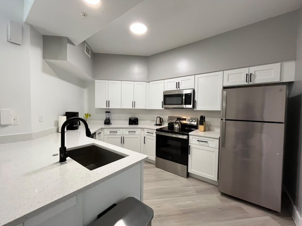 A modern kitchen with white cabinetry, stainless steel appliances, and a central island with a sink.