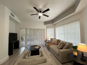 Ein modernes Wohnzimmer mit Deckenventilator, Sofa, Couchtisch und Fernseher.