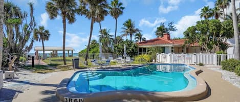 A swimming pool with a 3 ft 6 in depth, surrounded by palm trees and a building with a red-tiled roof.