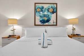 Ett hotellrum med en säng, två sängbord, ett litet bord, en tavla som hänger på väggen och en digital klocka.