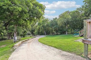 Ein unbefestigter Weg schlängelt sich durch einen Park mit Bäumen und einer Holzkonstruktion auf der rechten Seite.