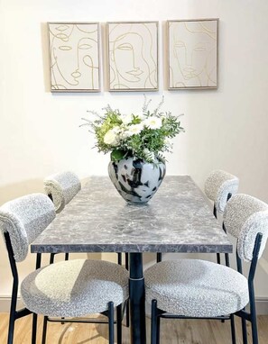 Une table à manger ornée d’un vase de fleurs, entourée de six chaises dont les assises sont revêtues d’un tissu texturé.