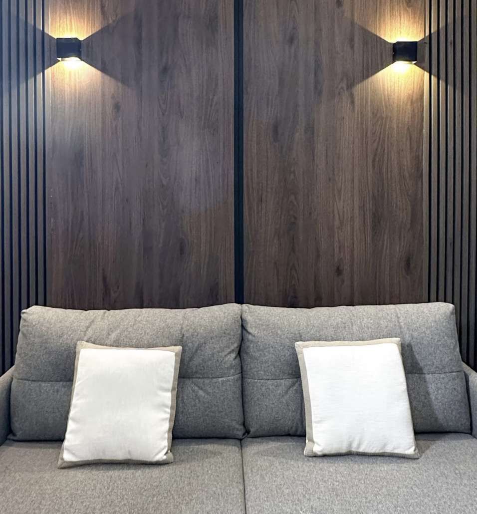 Un sofá con dos almohadas frente a una pared de listones de madera y dos luces instaladas en la pared.