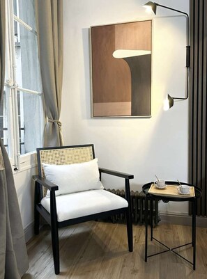 A room with a chair, a table with a tray, a wall-mounted lamp, and a window with curtains. - Superb Appartment close to Marais by Melvane 4P (Paris)
