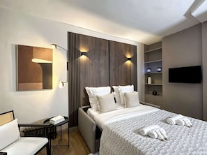 Une chambre d’hôtel comprenant un lit, des tables de chevet, une chaise, un téléviseur et une étagère fixée au mur.