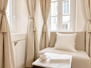 A room with a sofa, a table with a cup and a book, and curtains tied back. - Saint Germain Deluxe Studio by Melvane (Paris)