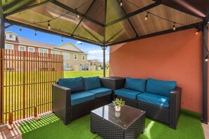 Ein Sitzbereich im Freien mit einer überdachten Terrasse, einem Holzzaun und Blick auf Wohnhäuser.