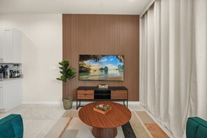 Una sala de estar moderna con un televisor de pantalla plana, una mesa de comedor y una cocina al fondo.