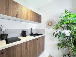Eine moderne Küche mit Holzschränken, einem schwarzen Spülbecken, einer Kaffeemaschine und einem Blumentopf.