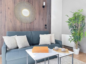 Ein modernes Wohnzimmer mit einem grauen Sofa, einem weißen Couchtisch, einer Louis Vuitton Box, einem Ziertegelspiegel und einer Bambuspflanze.