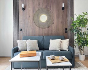 A modern living room with a grey sofa, two side tables, a decorative wall piece, and a potted plant. - Cozy studio Louvre, Saint Honore by Melvane (Paris)