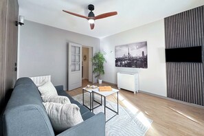Een moderne woonkamer met een grijze bank, een plafondventilator, een stadslandschap schilderij en een radiator.